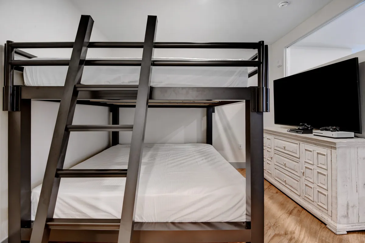 The image features a bunk bed setup, a television, and a dresser, with a playful and inviting ambiance. This setup is ideal for families, children, or groups, offering both sleep and entertainment in a cozy space.
