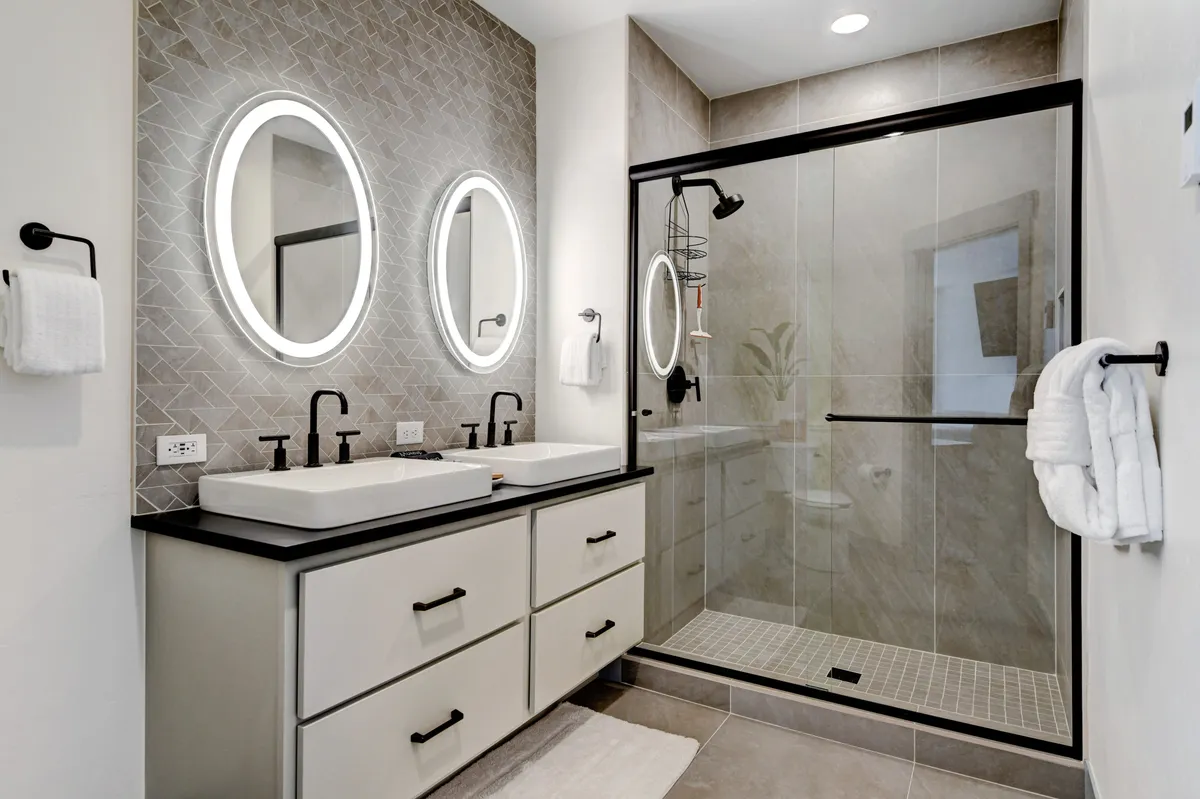 This bathroom image highlights dual sinks with large mirrors, a walk-in glass shower, and textured wall tiles. The overall mood is sleek and serene, evoking a spa-like atmosphere for relaxing daily routines.