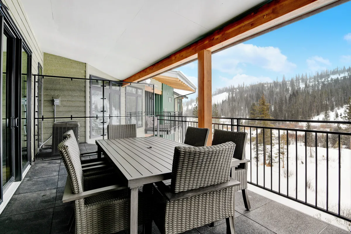 A cozy outdoor dining setup with wicker chairs and a table, set against a snowy landscape and mountain views, inviting moments of relaxation after a day of adventure. The scene captures the transitional space between indoor comfort and the great outdoors.