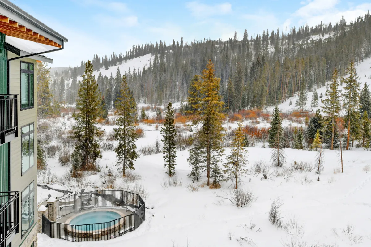 A serene setting featuring a steaming hot tub framed by snow, pine trees, and mountain vistas. The atmosphere promotes relaxation and family togetherness, with plenty of space for groups to enjoy the winter landscape.