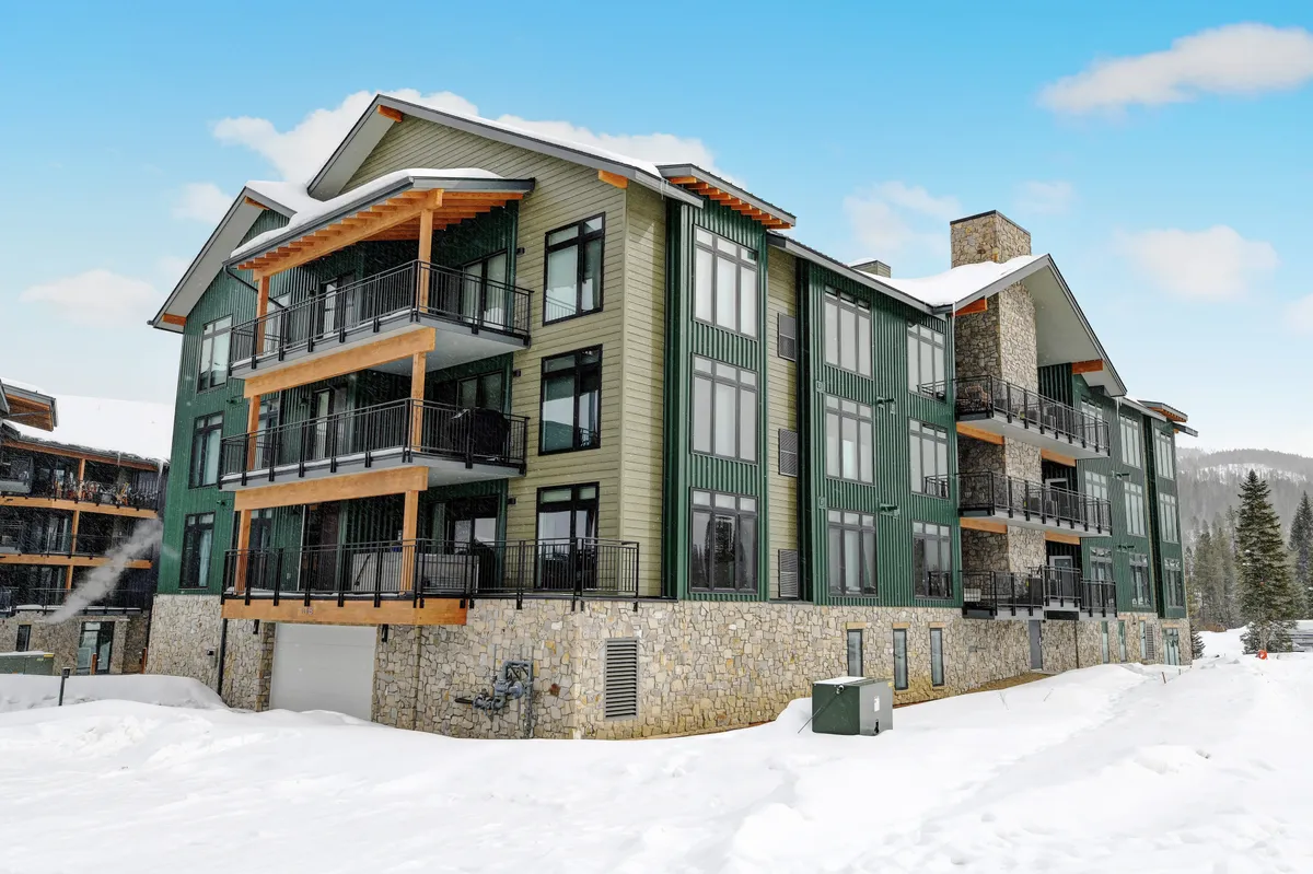 This exterior image showcases the property’s green and stone facade, accented by large windows and balconies. The snowy mountain backdrop and the inviting atmosphere evoke the excitement of winter sports and alpine excursions.