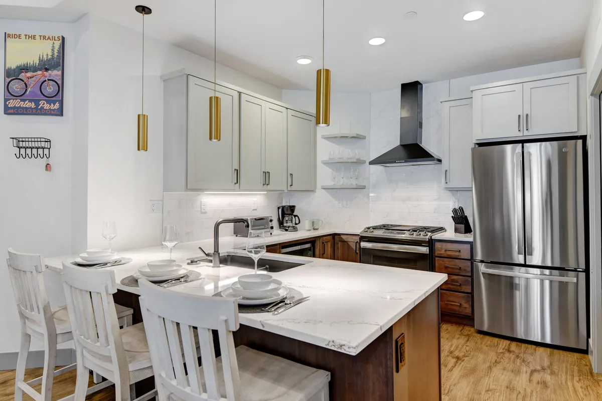 A contemporary kitchen scene with a gleaming kitchen island, stainless steel appliances, and elegant pendant lighting. The island offers bar seating, and the overall space is clean, modern, and designed for both cooking and socializing.