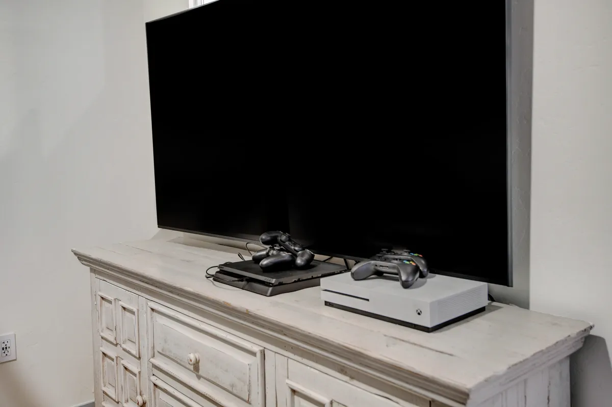 This image centers on a TV and gaming consoles set within a modern entertainment setup. Cabinets provide storage for games and accessories, and the scene conveys a space designed for playful, competitive gaming sessions or relaxed group hangouts. The overall mood is light-hearted and family-friendly.