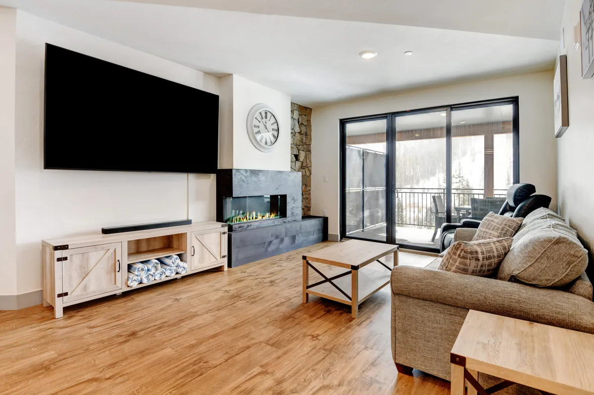 A cozy, modern living area with a large flat-screen TV, modern fireplace, and ample seating, set beside large glass doors that open onto a balcony. The space is perfect for group gatherings, game nights, or sharing stories after a day of exploration.