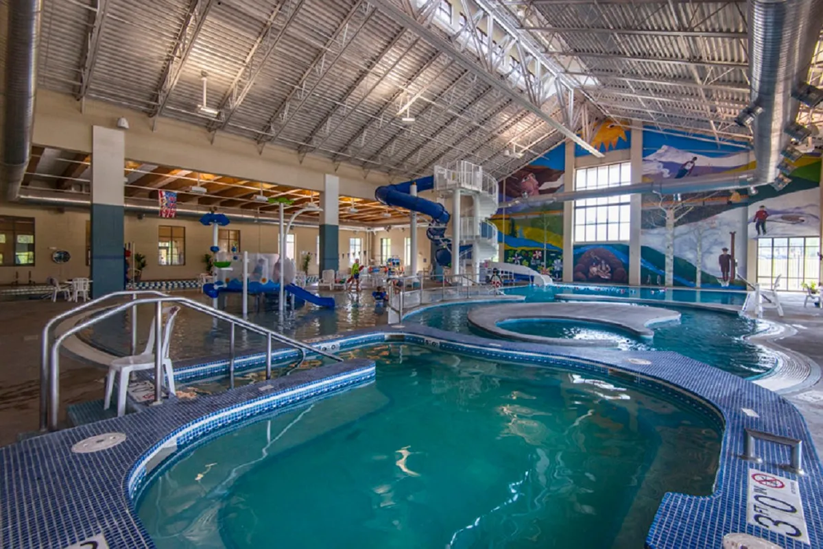 A bright, lively indoor recreation center features water slides, a large swimming pool, colorful murals, and children playing. The environment is fun and family-friendly, illustrating the range of activities available to guests beyond the residence itself.