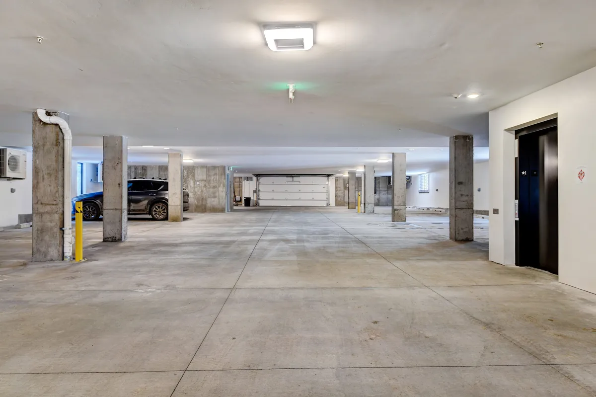 A view of secure indoor parking with clearly marked spaces, decorative columns, an elevator, and a garage door, creating a sense of easy access and arrival. The area is functional and welcoming, embodying the convenience of having vibrant activities just steps away from home base.