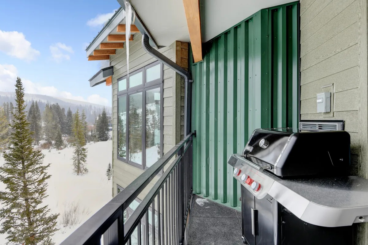 A cozy, covered balcony featuring a grill and dining table, surrounded by tall trees and offering relaxing views. The tableau suggests comfort and tranquility, ideal for both summer afternoons and snowy evenings. The balcony is perfectly suited for outdoor meals, barbecues, and unwinding after a day of mountain adventures.